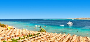 Blauwe zee en wit zandstrand met ligbedden en parasols in Egypte