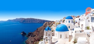 Witte huizen en kerkjes met blauwe koepels gebouwd tegen de berg op Santorini, Griekenland