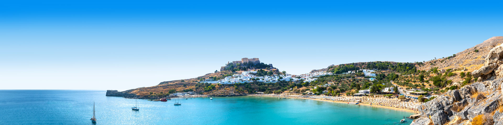 Een berg en blauw zeewater met bootjes tijdens de paasvakantie Rhodos